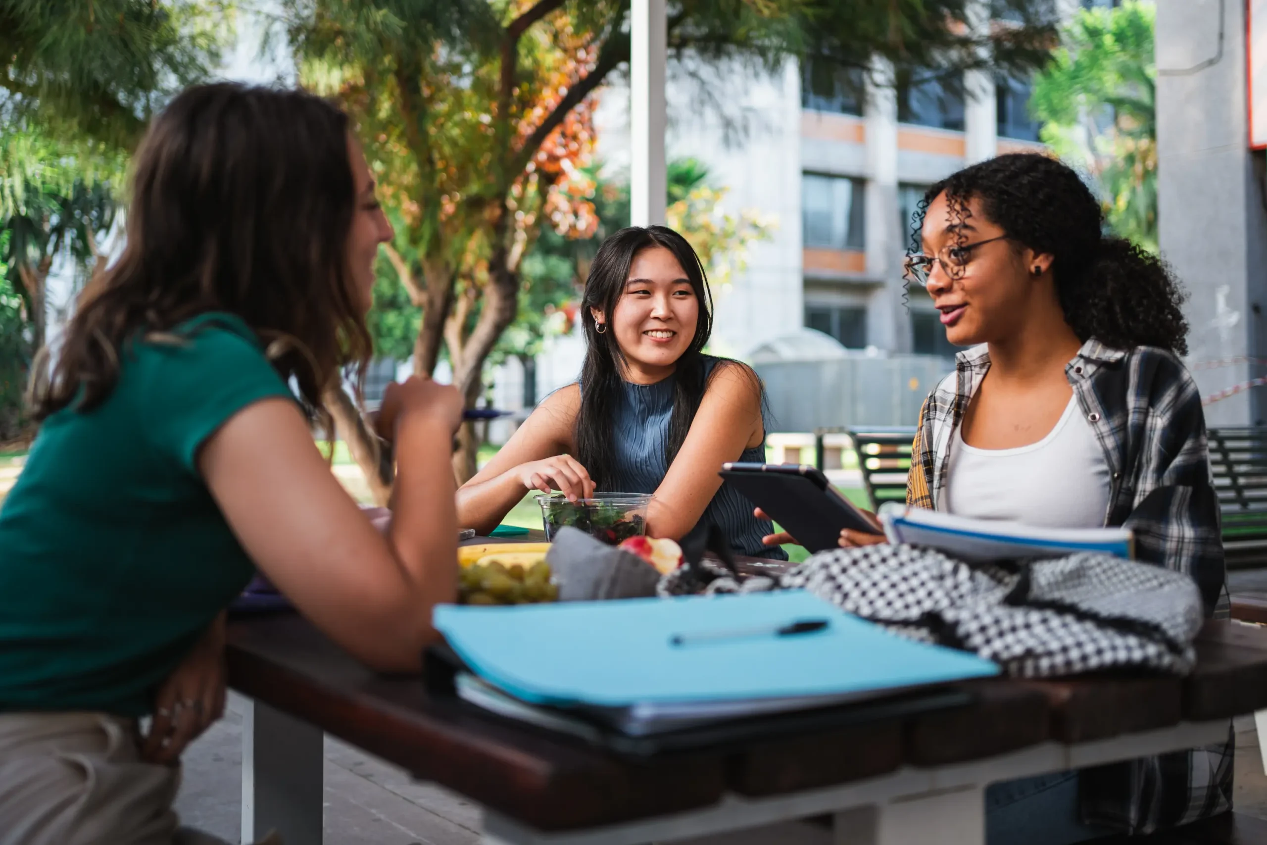 Three students studying together at an outdoor table on campus.